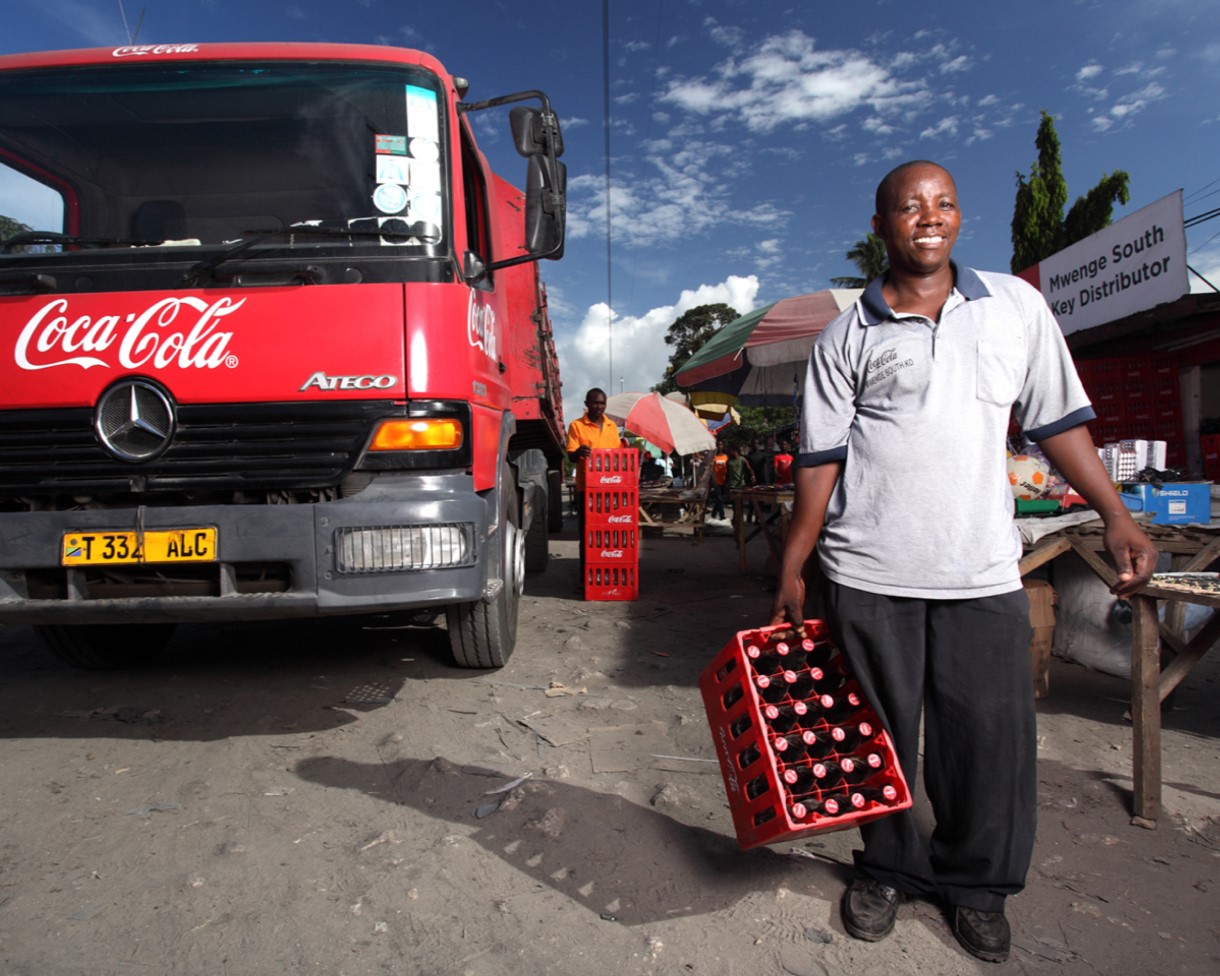 An employee of a key distributor standing at a Coca-Cola truck and holding a case of glass Cokes bottles