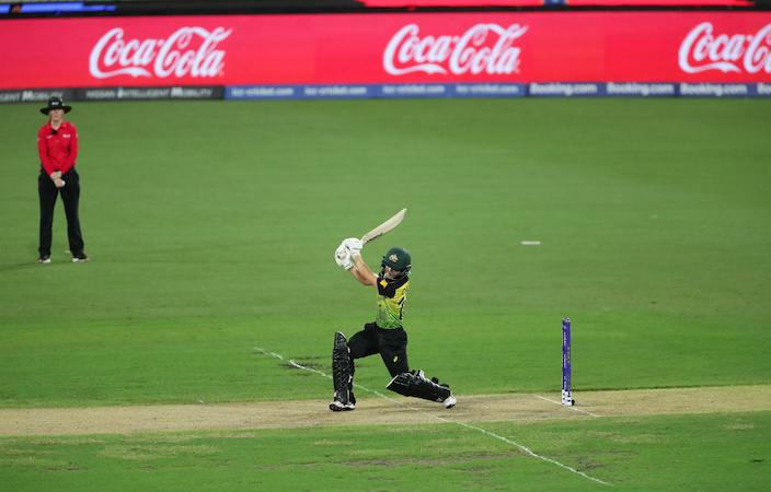 Cricket player on the field with a Coca-Cola banner in the background