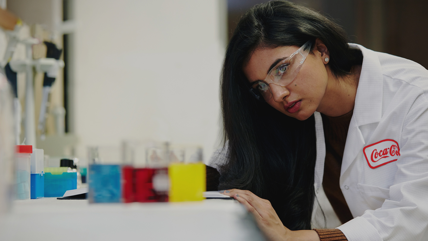 A woman in a Coca-Cola lab coat inspects colorful liquids