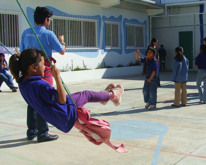 A girl swings as a teacher and students talk and play around her